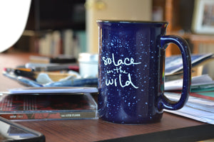 Blue ceramic Solace in the Wild mug on Erin's desk.